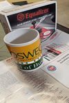 A Oswego School of Business coffe cup sitting ontop of a AGRR Magazine July August 2019 
issue with a Equalizer Rain Sensor Level Part number RSK330 in the back ground.